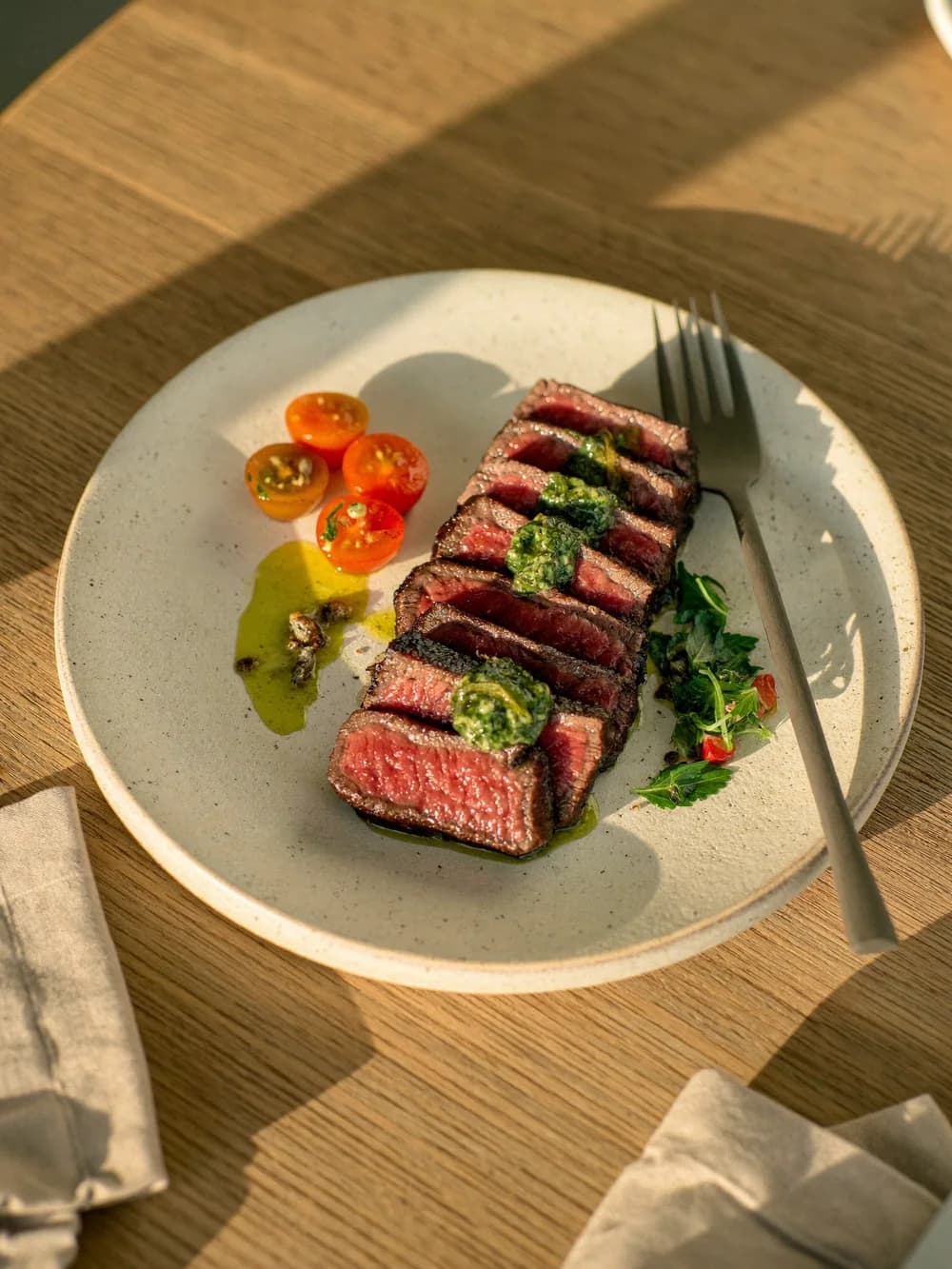 Seared sliced steak with chimichurri and cherry tomatoes on a speckled plate